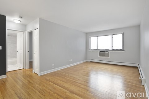 A spacious room with wooden flooring and a window with blinds.