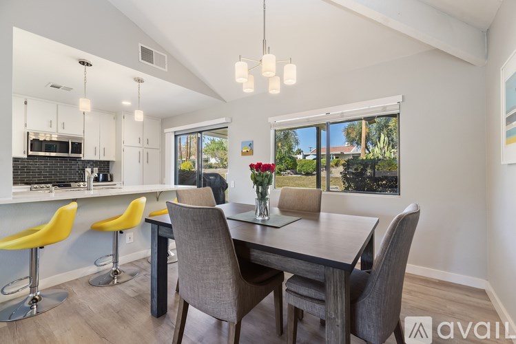 A modern dining room with a table set for two and a kitchen area in the background.