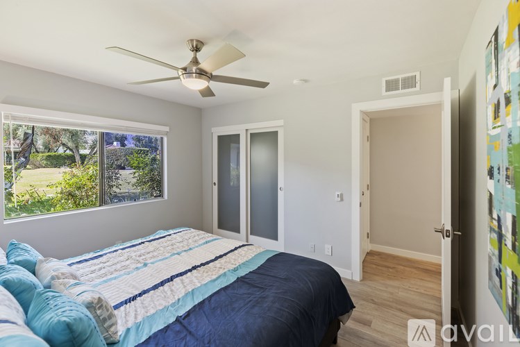 A bedroom with a bed, a ceiling fan, and a window overlooking a garden.