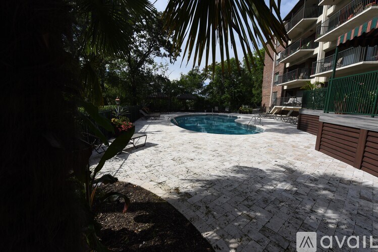 A pool surrounded by a brick patio and greenery.