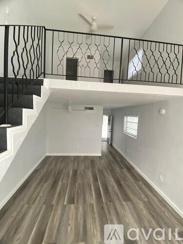 A spacious room with wooden floors and a balcony with black railings.
