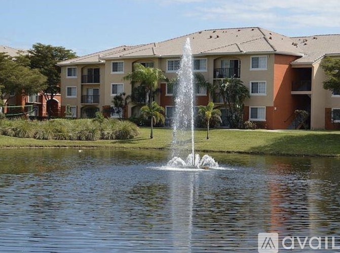 A fountain in the foreground of a grassy area in front of apartment buildings.
