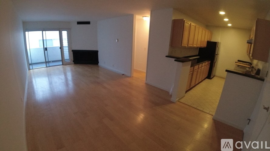 A spacious living room with wooden floors and a kitchen area with white cabinets.