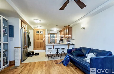 A living room with a blue couch and a kitchen area in the background.