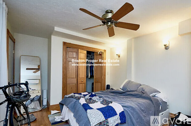 A bedroom with a bed, a fan, and a bicycle.