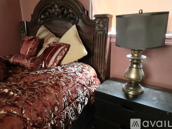A bed with a red and gold comforter and a lamp on a side table.
