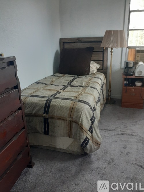 A bed with a striped comforter is in a room with a lamp and nightstand.