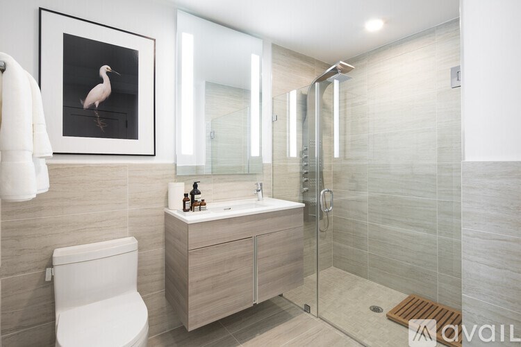 A bathroom with a white toilet, a sink with a cabinet, a shower with a glass door, and a picture of a bird on the wall.