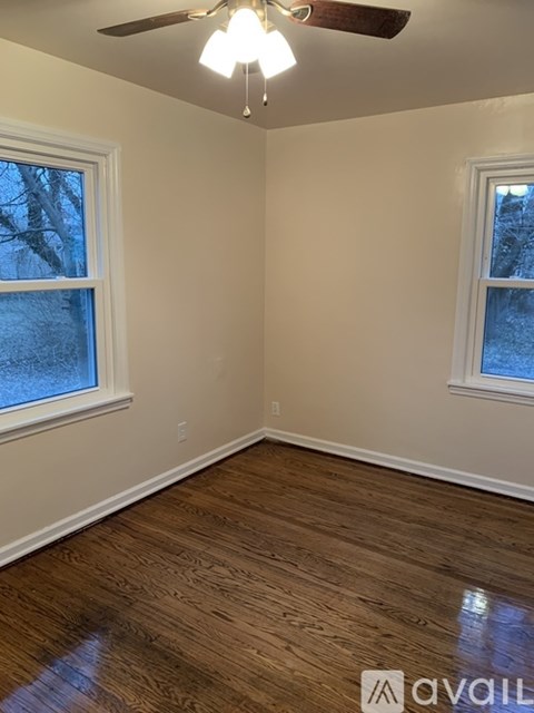 A room with a ceiling fan and two windows.