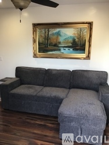 A grey couch with a painting of a lake and trees above it.