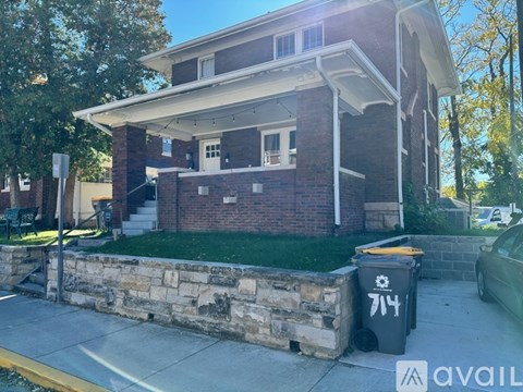 A house with a stone wall and a trash can in front.