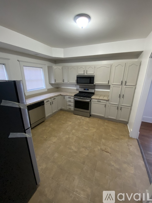 A kitchen with a black fridge, white cabinets, and a microwave.
