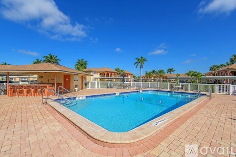 A large outdoor swimming pool surrounded by a brick patio and a white fence.