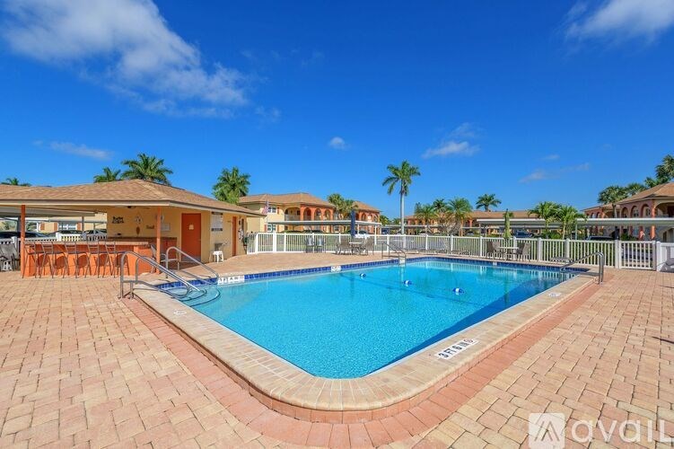 A large outdoor swimming pool surrounded by a brick patio and a white fence.