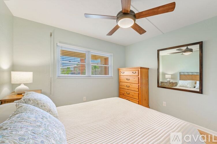 A bedroom with a large bed, a ceiling fan, and a dresser with a mirror above it.