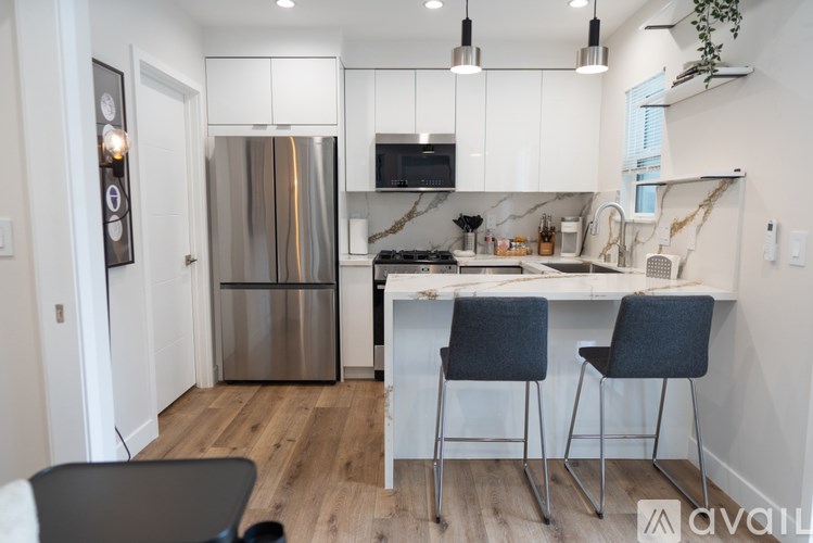 A kitchen with a refrigerator, stove, and two chairs.