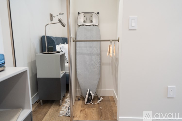A room with a white wall and a grey ironing board.