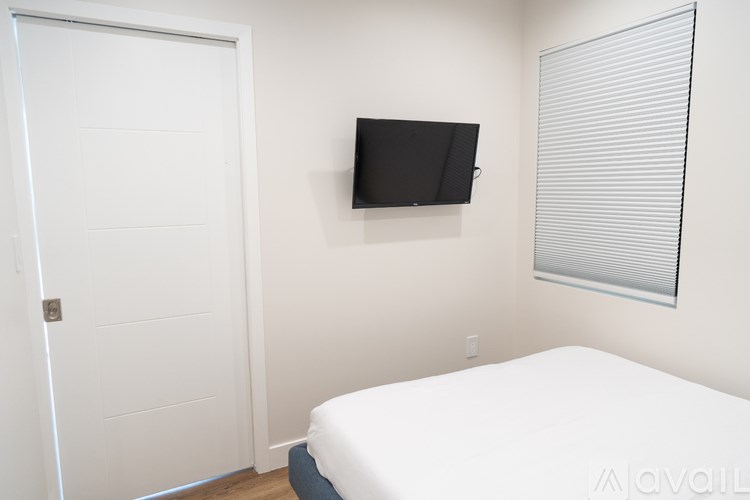 A bedroom with a bed, a door, and a television mounted on the wall.