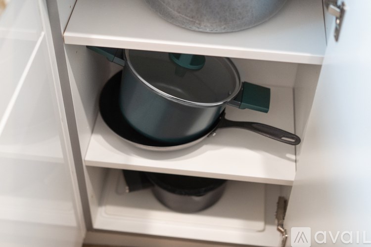 A pot with a black lid and handle is sitting on a white shelf.