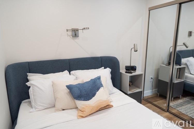 A bed with a blue headboard and white pillows is in a room with a mirror and a nightstand.