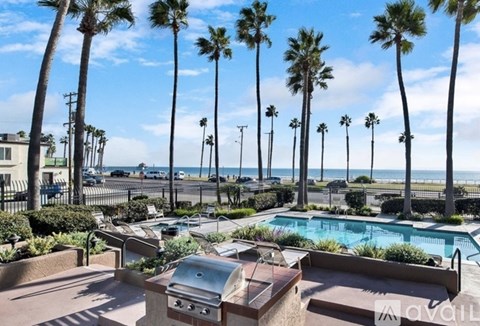 A backyard with a pool, grill, and palm trees.