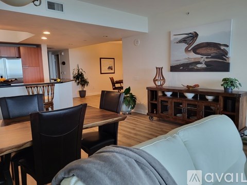 A living room with a dining table and chairs, a painting of a pelican, and a cabinet with bowls on it.