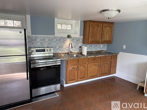 A kitchen with a stainless steel refrigerator and oven, wooden cabinets, and a marble backsplash.