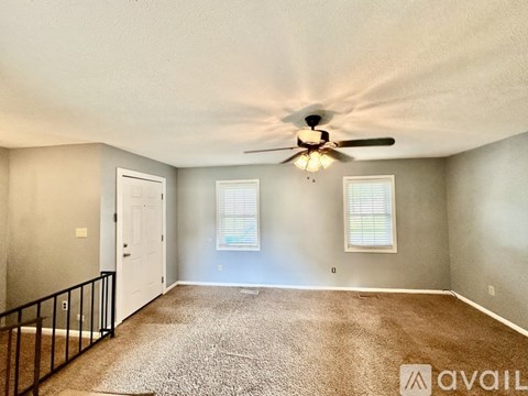 A spacious room with a ceiling fan and two windows.