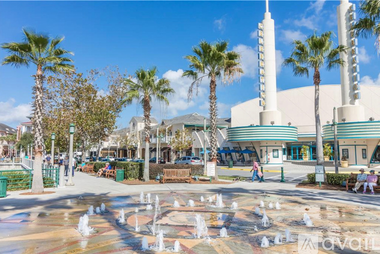 A fountain in the middle of a plaza with palm trees and a building in the background.