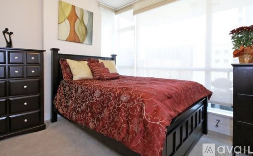 A bedroom with a red bedspread and a black dresser.