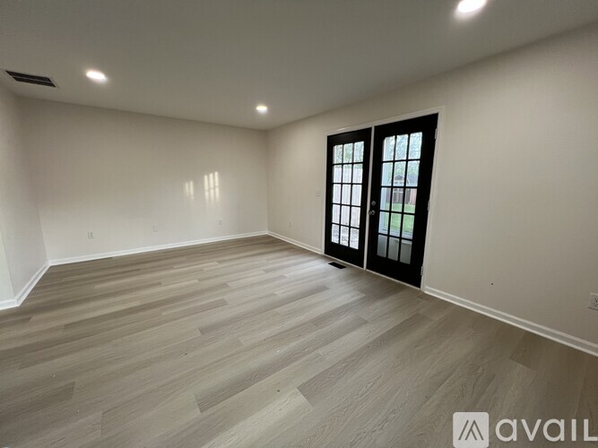 A spacious room with wooden flooring and a large window with black frames.