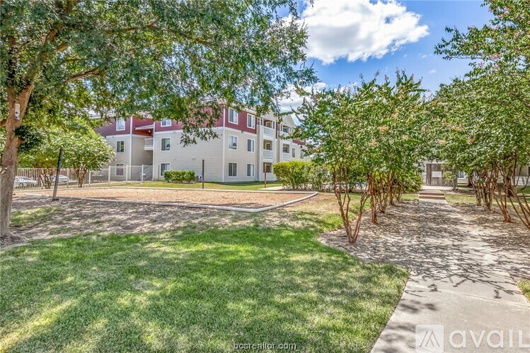 A sunny day at a grassy courtyard with trees and apartment buildings in the background.