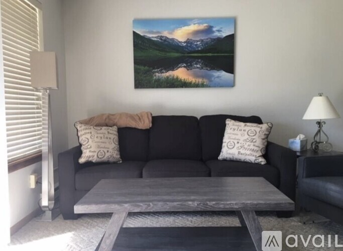 A living room with a black couch and a painting on the wall.