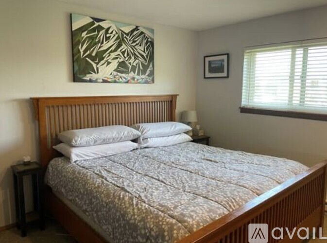 A bedroom with a bed, nightstand, and a painting on the wall.