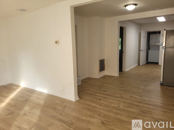 A spacious room with wooden flooring and a refrigerator in the corner.