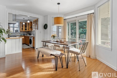 A dining area with a table and chairs in the foreground and a kitchen area in the background.