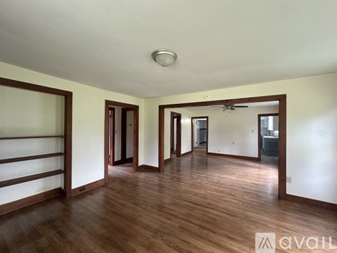 A spacious room with wooden floors and white walls, featuring a ceiling fan and a large mirror.