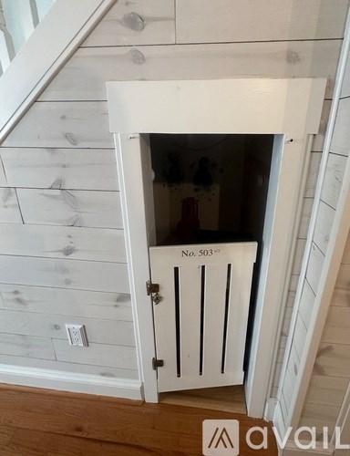 A white door with a black handle is open to a room with wooden walls.