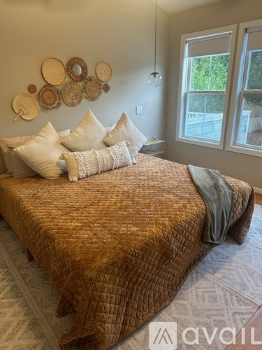 A bed with a brown comforter and pillows is in the foreground of a room with a window and wall decorations.
