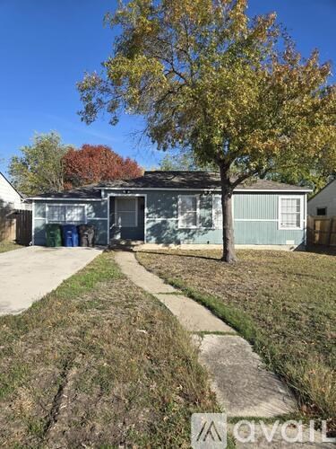 A tree with yellow leaves stands in front of a grey building.