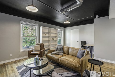 A living room with a brown leather couch, a glass coffee table, and a window with a view of trees.