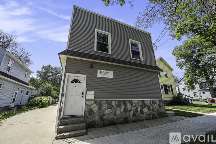 A two-story house with a grey facade and a white door is for sale.