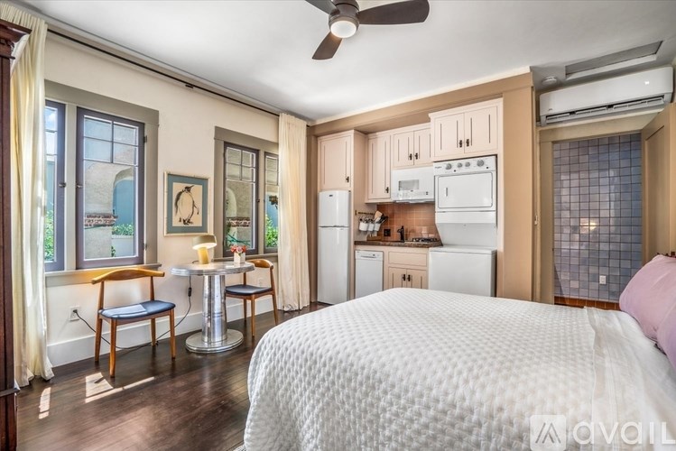 A bedroom with a bed, a table and chairs, and a kitchen area with a refrigerator, microwave, and oven.