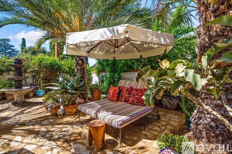 A patio with a striped cushioned bench and a white umbrella.