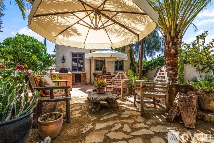 A patio with a white umbrella and wooden furniture.
