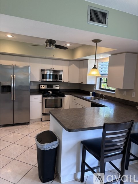 A kitchen with a black chair and a black trash can.