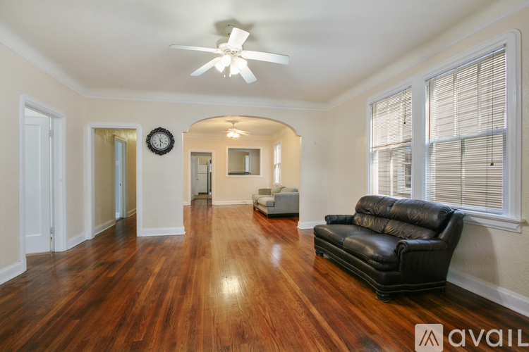 A living room with a black leather couch and wooden floors.