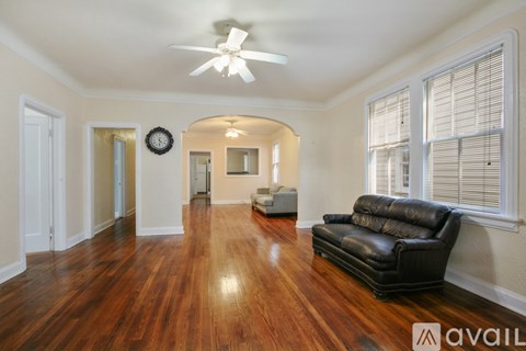 A living room with a black leather couch and wooden floors.