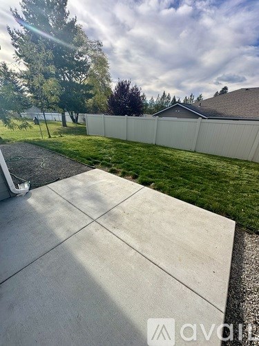 A concrete patio leads to a white fence and green lawn.