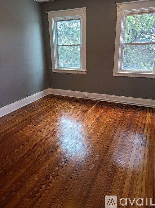 A room with wooden flooring and two windows.